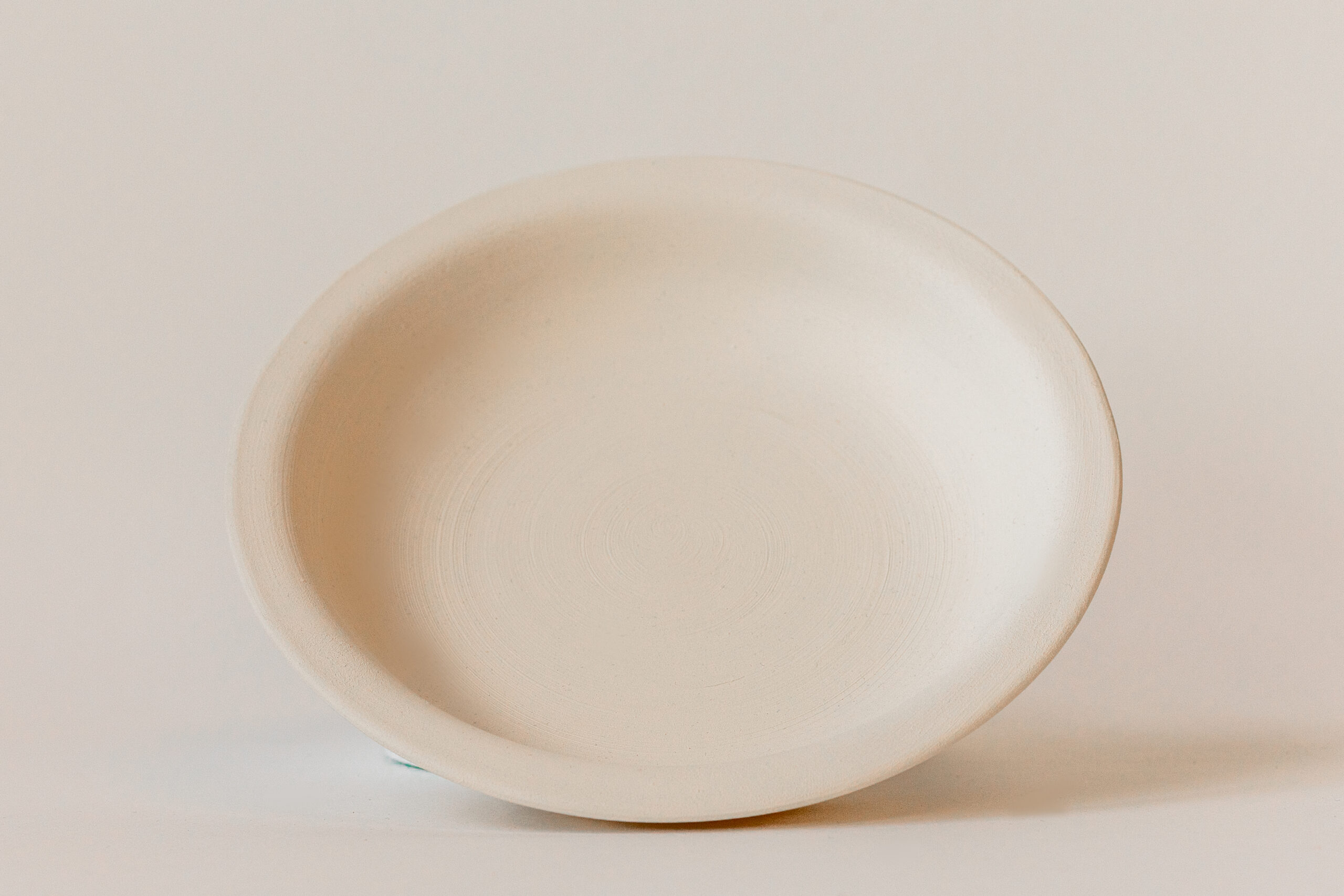 Un bol ovale peu profond, de couleur crème et vide, repose légèrement incliné sur une surface claire, devant un fond uni.