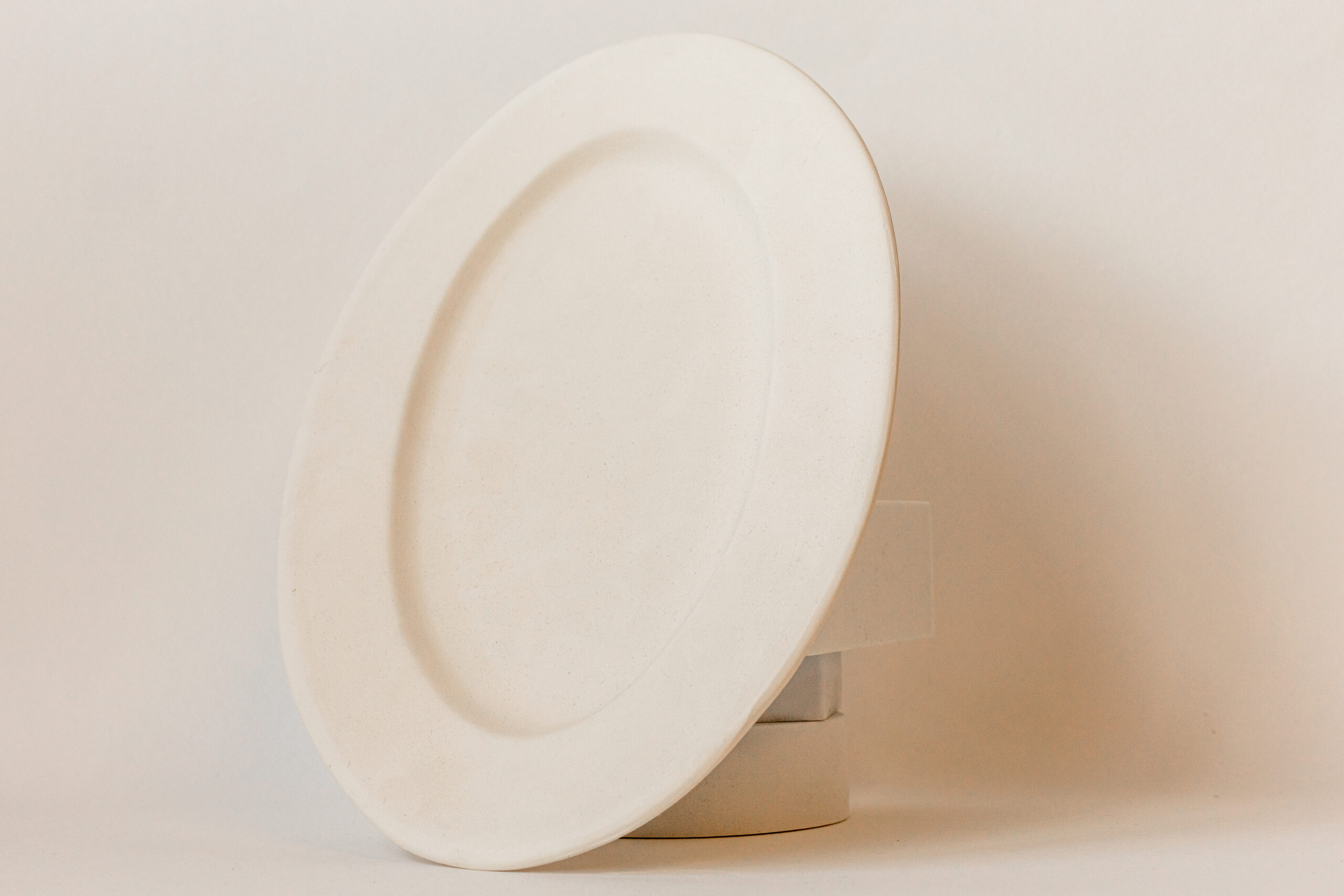 Une assiette ovale claire se dresse verticalement, légèrement inclinée, sur un fond uni et lumineux.